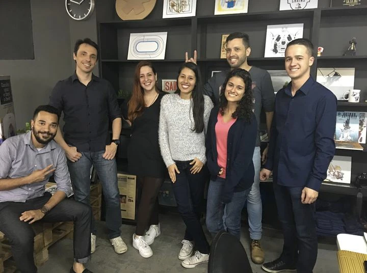 Equipe do Por Acaso e do Aconteceu em Jaraguá reunida na redação, com o asterisco e a coluna impressa emoldurada na estante